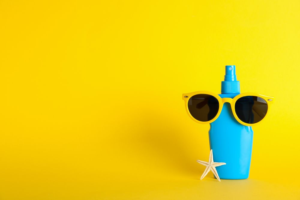 Sunscreen spray with starfish and sunglasses on color background, space for text