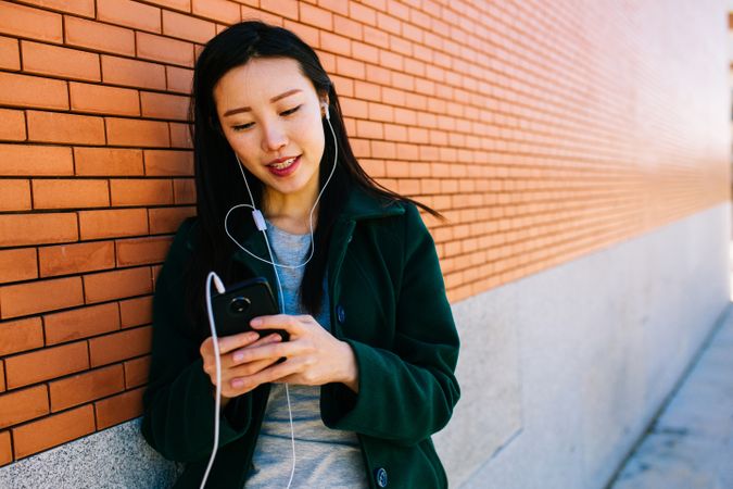 Asian female listening to music near brick wall