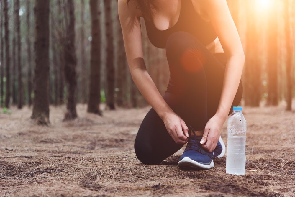 Woman sitting on forest floor tying shoes with sun flare