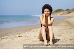Woman sitting in sand on the beach looking at camera beEJNb
