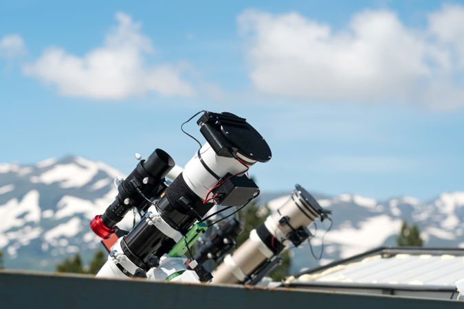 Telescopes on observatory rooftop with mountains and blue sky.
