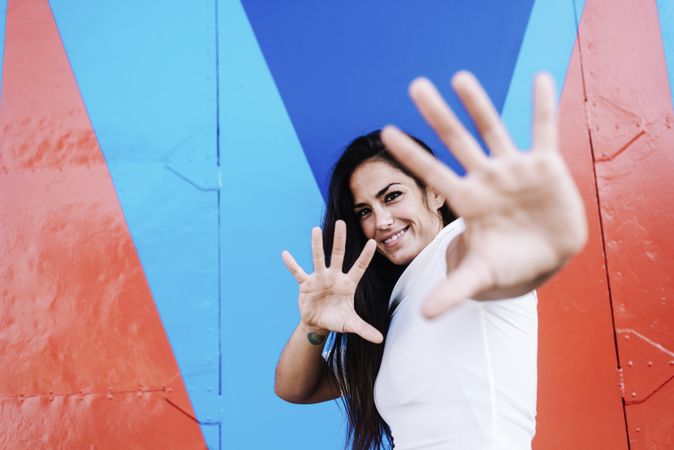 Portrait of a young smiling woman gesturing with hands while looking to camera against a colored wall