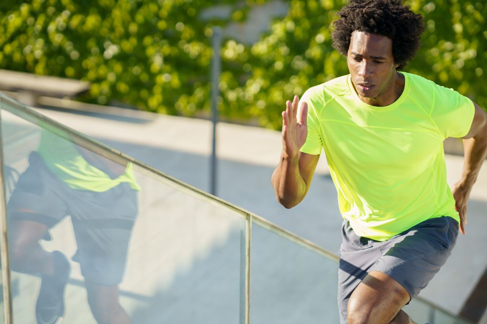 Healthy man in neon T-shirt doing cardio on outdoor staircase