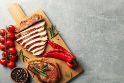 Board with fried steaks on gray background. Grilled food