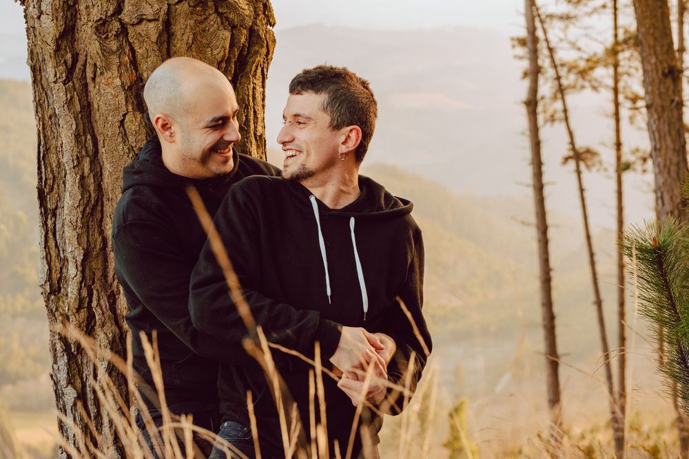 Smiling men hugging near tree in forest on hill