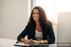 Businesswoman with curly hair in formal clothes sitting at her desk in office 5pJyOb