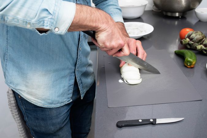 Man prepping onion on board with knife