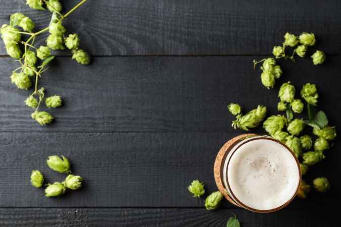 Glass of beer and hop cones on wooden background, top view