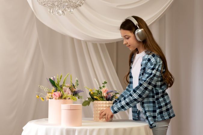 Teen girl with headphones arranging flowers on decorated table.