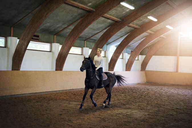 Female horse rider taking her mare for a ride in an indoor arena