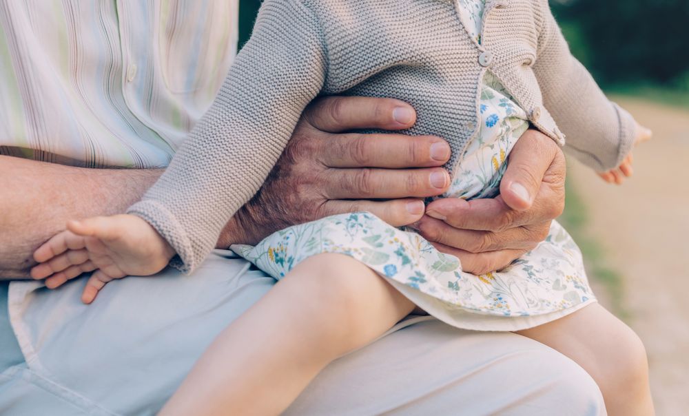 Baby girl sitting over legs of grandfather outdoors