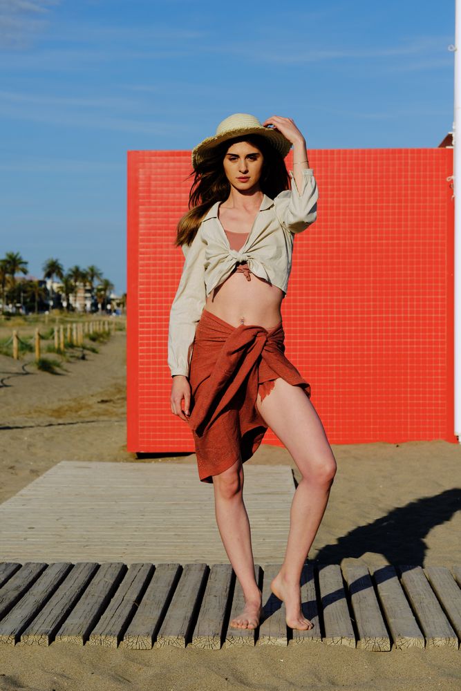 A long hair fashion model with a hat at the beach in front of a red wall