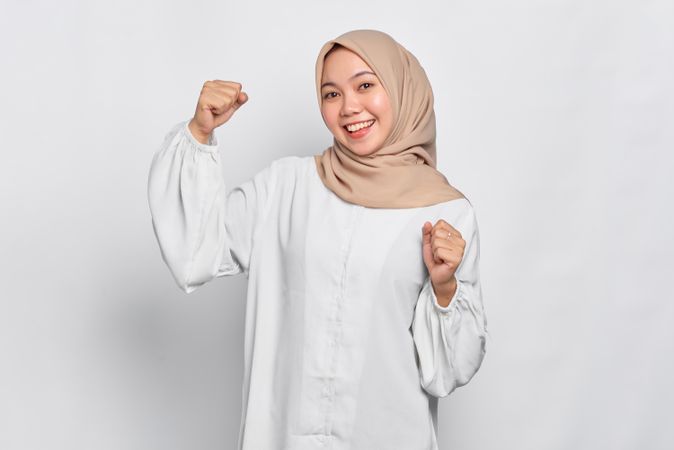 Giddy Muslim woman in headscarf in light blouse with hands up in celebration