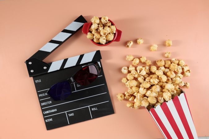 Tasty Popcorn in Paper Buckets, Movie Clapper and 3D Eyeglasses on a Bright Colored Background.