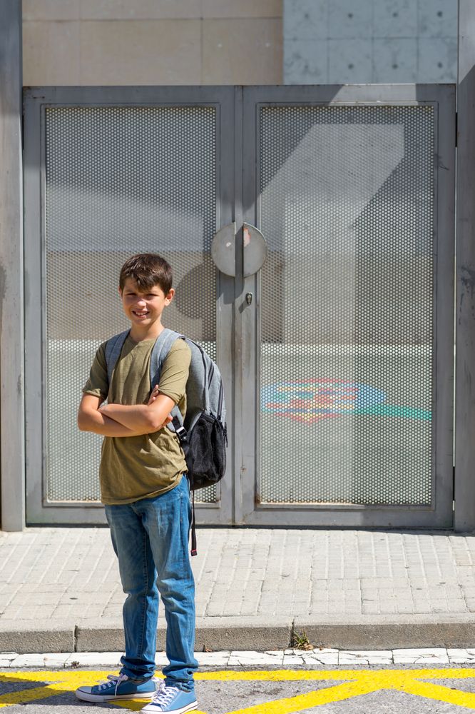 Proud child carrying his backpack standing in front of the school