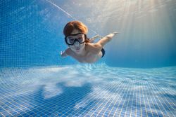 Small boy in mask swimming underwater of pool