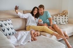 Mother and father taking selfie on smartphone near sleeping daug