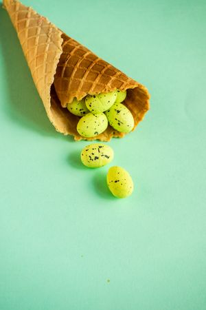 Waffle cone with small speckled eggs on green pastel background