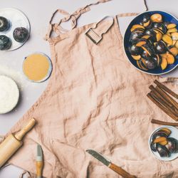 Baking ingredients and tools, plums, pastry brush, cinnamon, eggs on pink apron, square crop
