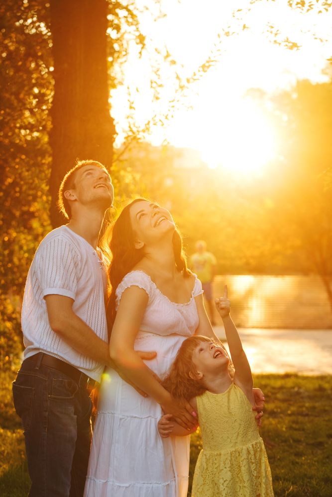 Young family looking up in park at magic hour with daughter pointing