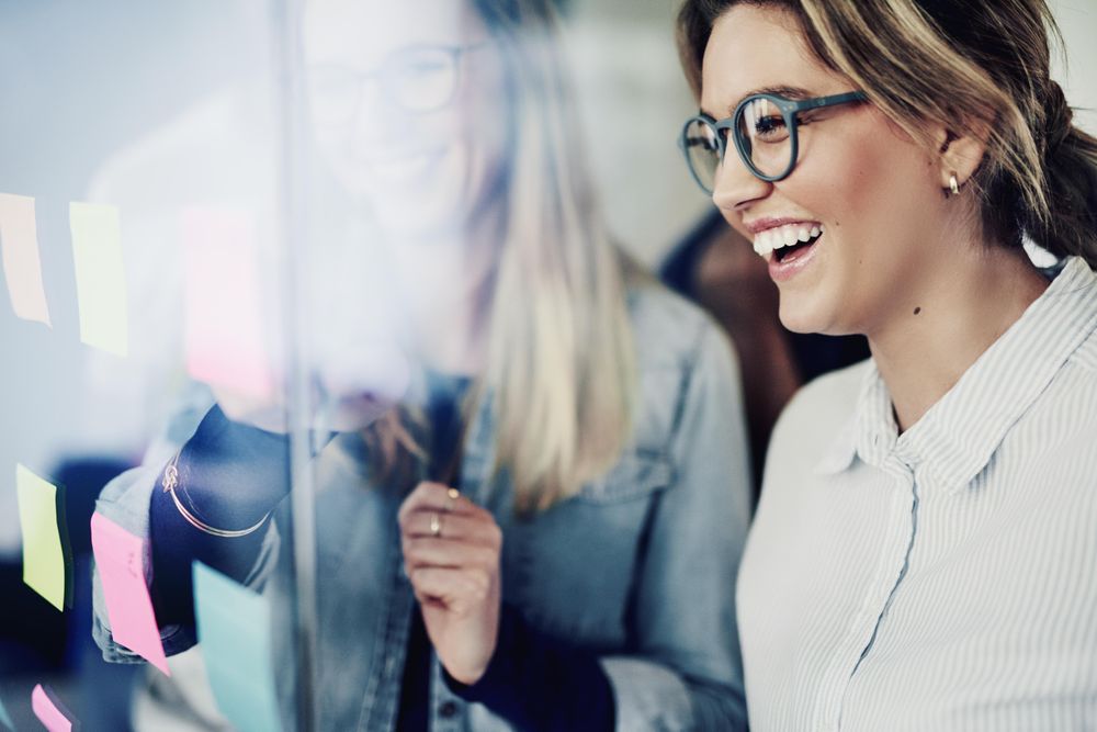 Two female colleagues laughing as they brainstorm with sticky notes
