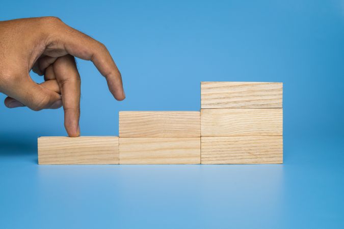 male hand walk on stairway wooden blocks isolated on blue background