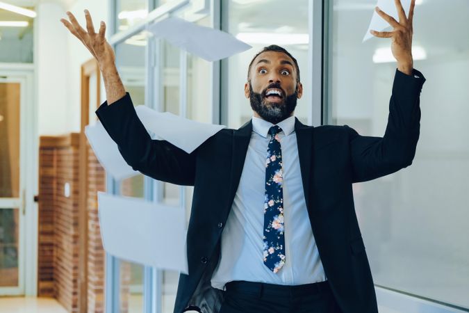 Surprised businessman in suit and tie throwing papers in the air in office