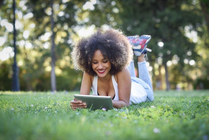 Carefree Black woman with afro hairstyle using digital tablet in park