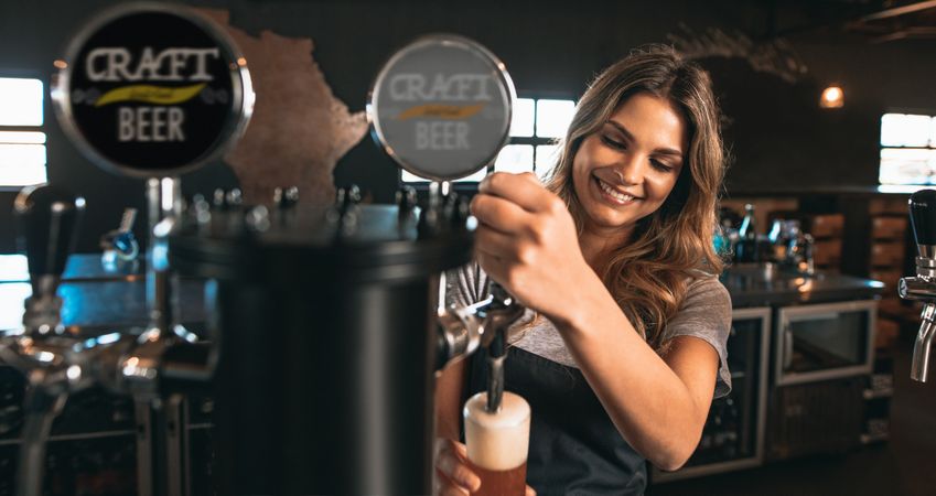 Beautiful young woman pouring beer into glass
