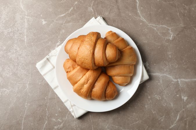 Plate with croissants on napkins on grey table, top view