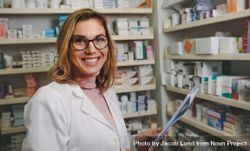 Happy female chemist wearing eyeglasses holding a prescription in drug store shelves 5oErxb