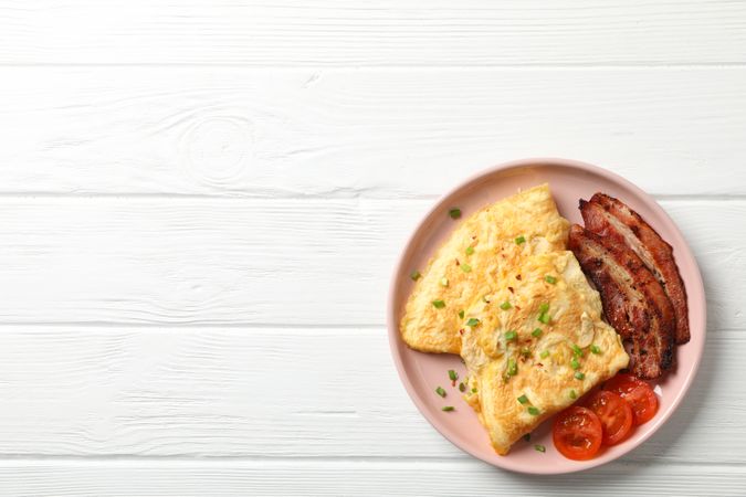 Breakfast of scrambled eggs and bacon on pink plate, copy space