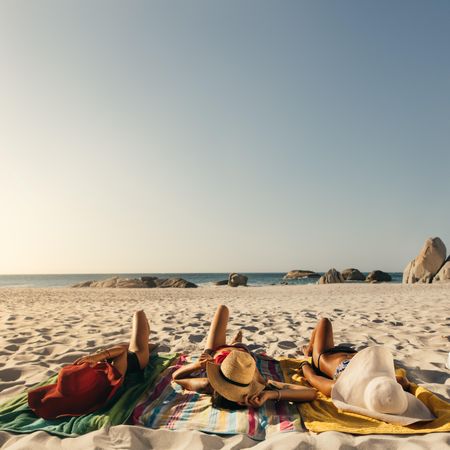 Rear view of women in bikinis sunbathing lying on beach wearing sunhats