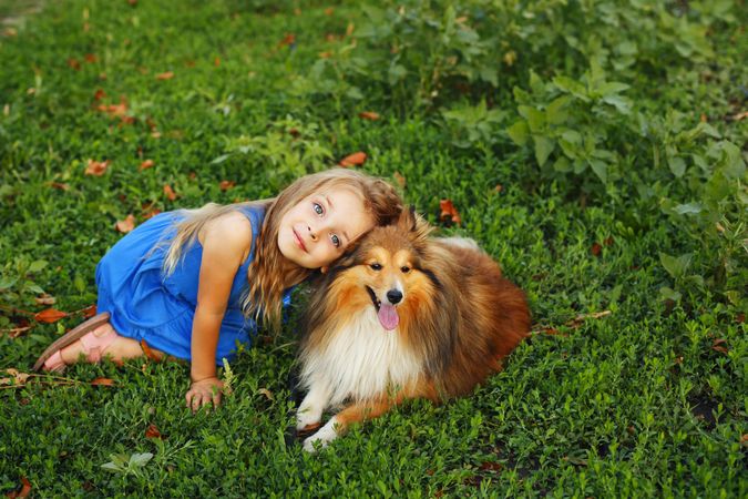Female child in blue dress looking up with dog in the grass