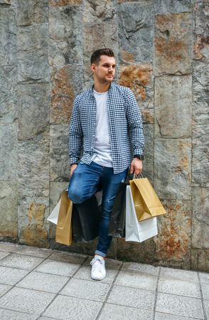 Young man with shopping bags leaning on wall