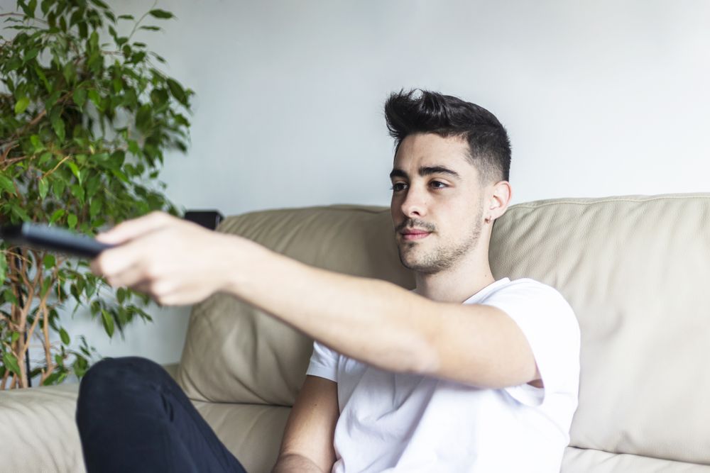 Happy young man on sofa with remote control watching TV