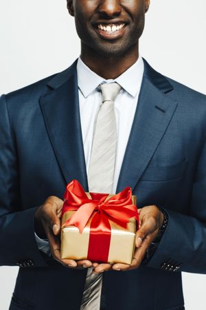 Image of cropped Black man holding present wrapped in gold paper and red bow