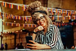 Black woman in stripe shirt smiling on video call in cafe