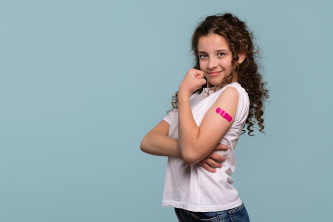 Girl flexing arm with pink bandage after vaccination