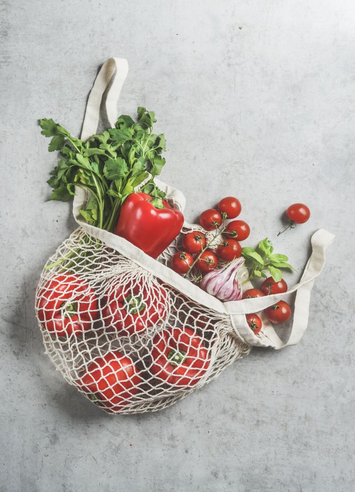 Top view of various vegetables and herbs in reusable plastic free shopping bag at grey concrete kitchen table