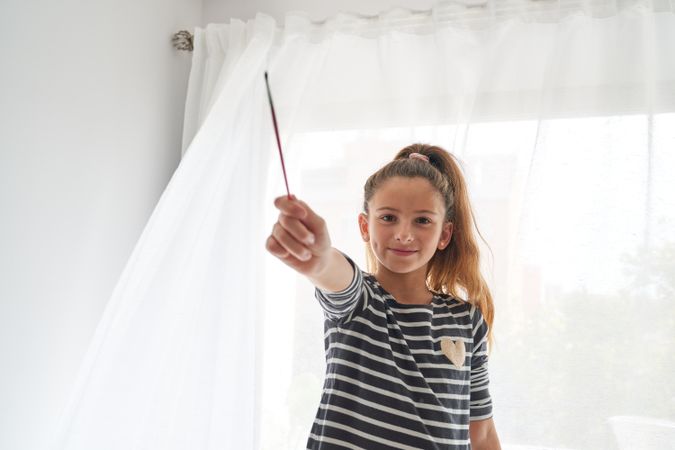 Smiling girl holding paintbrush in white room