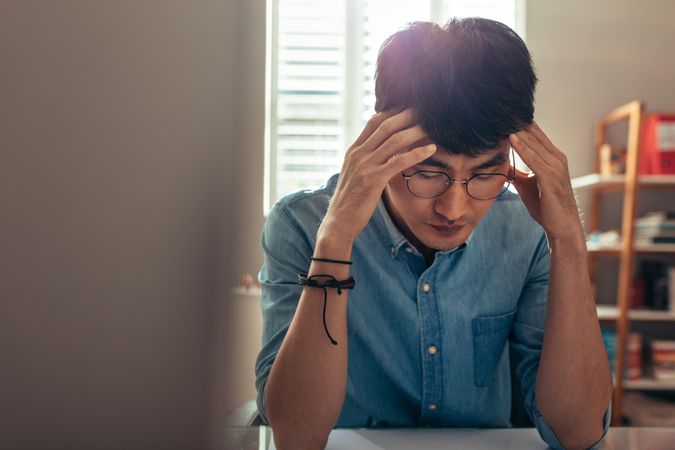 Man sitting at his desk at home with hands near his head trying to solve a problem