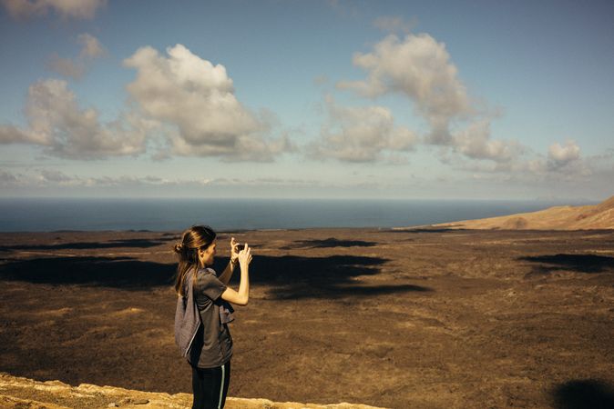 Side view of woman taking picture of vast terrain
