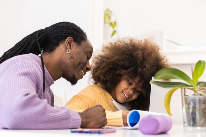 Black father helping daughter with homework on laptop
