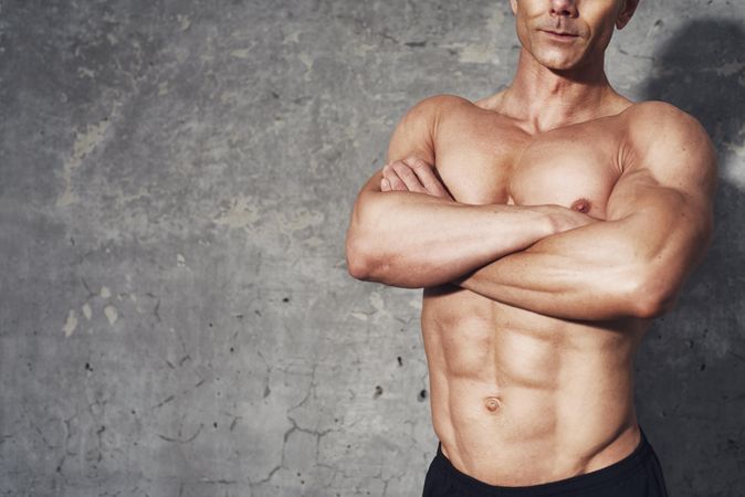 Portrait of muscular man’s torso with arms crossed against concrete wall