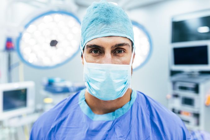 Close up portrait of male surgeon wearing surgical mask and scrubs in operation theater