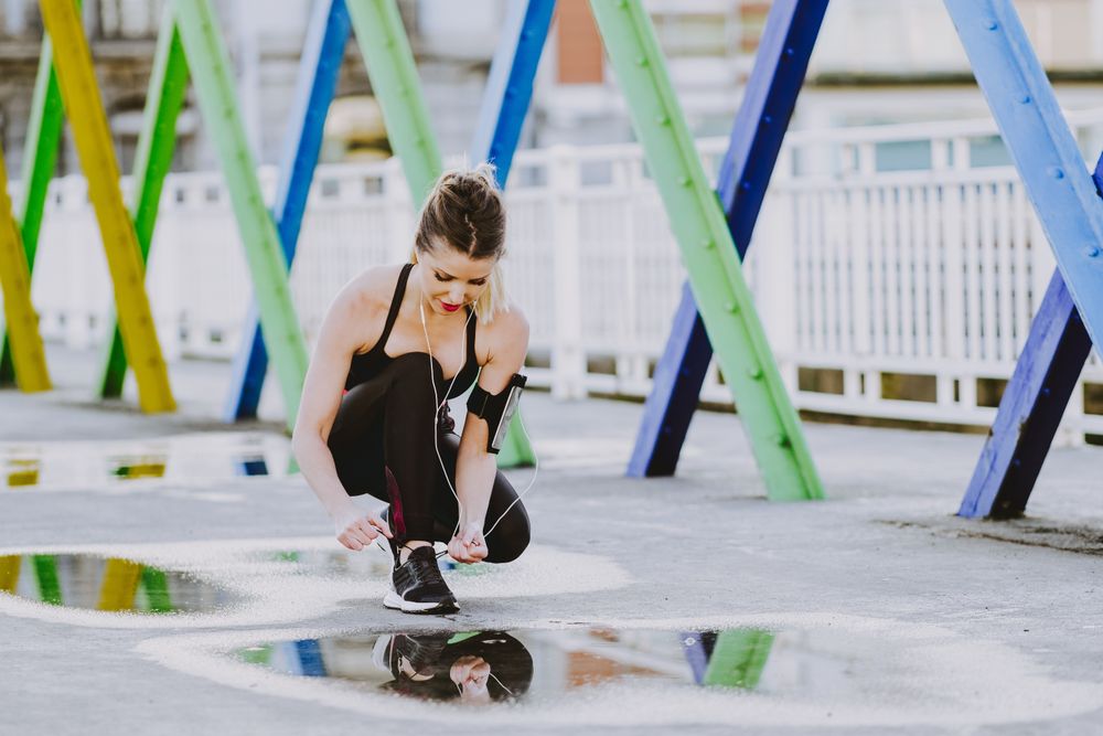Woman with earphones lacing shoes on street