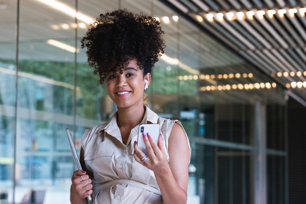 Smiling Black pregnant woman using smartphone and wireless earphones