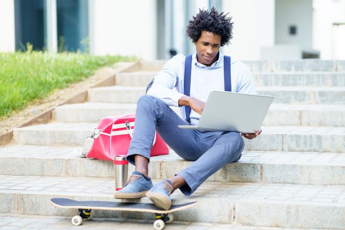 Man with laptop and skateboard sitting on outdoors steps