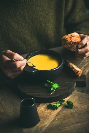 Man eating warm yellow soup from dark bowl holding toast